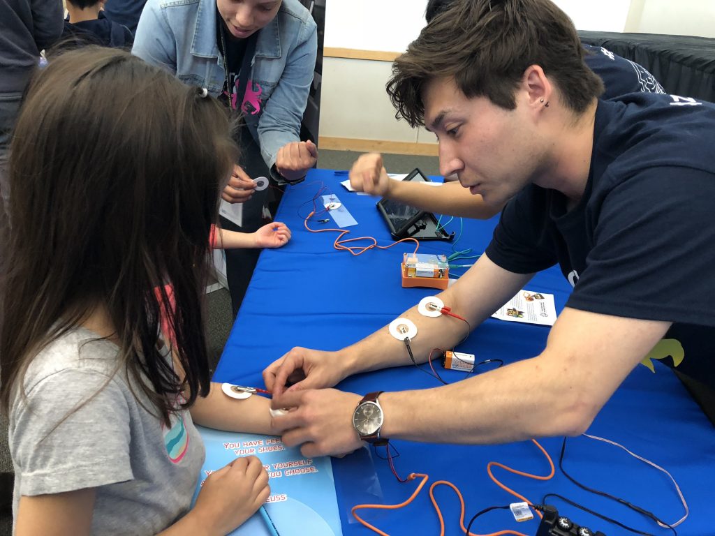 UCI Neuroscience Brain Ambassadors discuss current research in neuroscience - image of brain ambassador placing electrode on student's arm