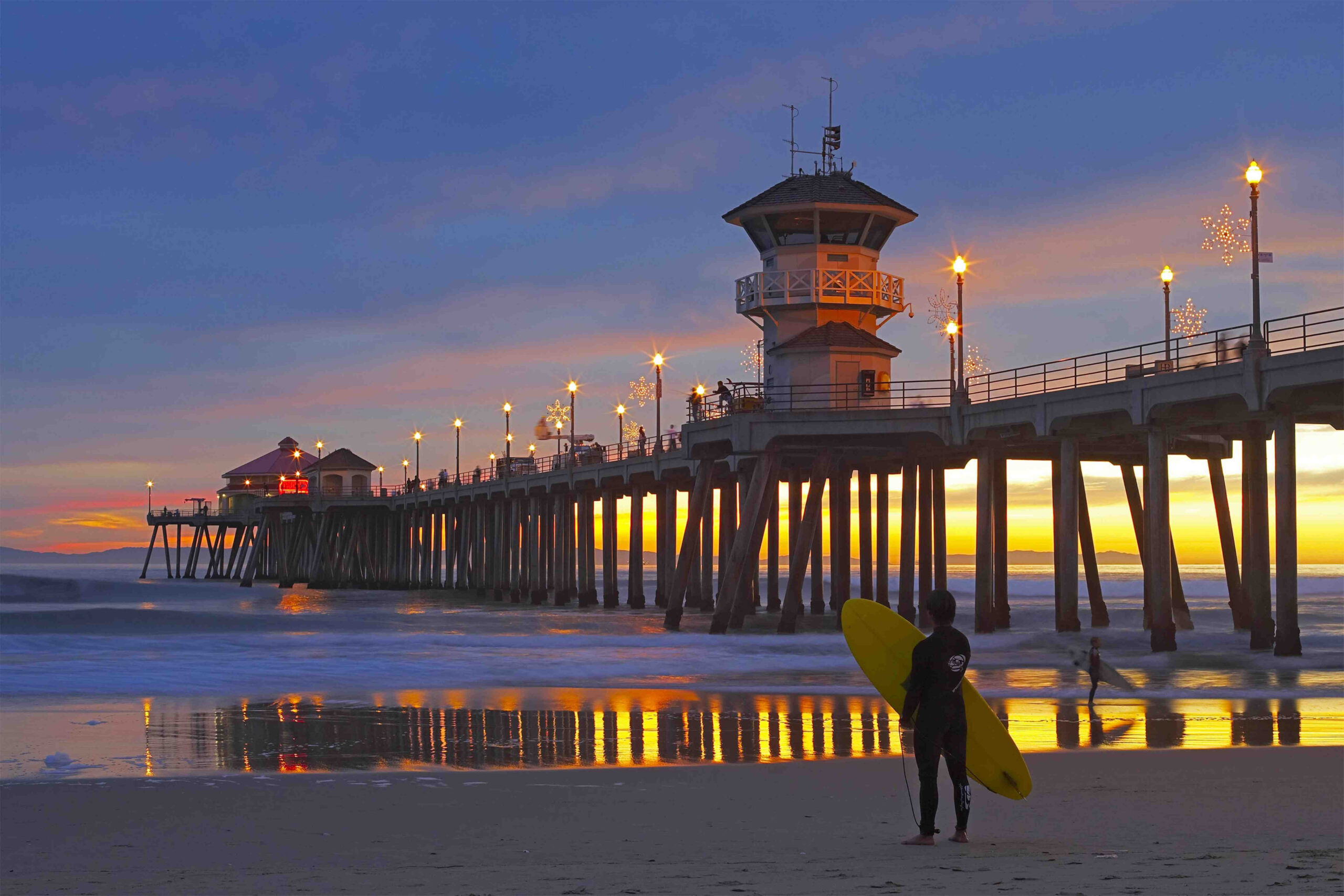 Surfer stands on beach in Huntington Beach at dusk