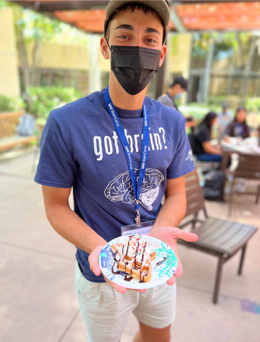 Aa student holds a waffle with whip cream and sprinkles to the camera